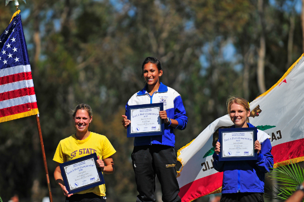 Drei Frauen, die Zertifikate halten und stehen, mit Flaggen und Bäumen im Hintergrund.
