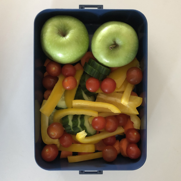 Eine blaue Lunchbox mit zwei grünen äpfeln, Tomaten, Gurken und anderen Obst und Gemüese.