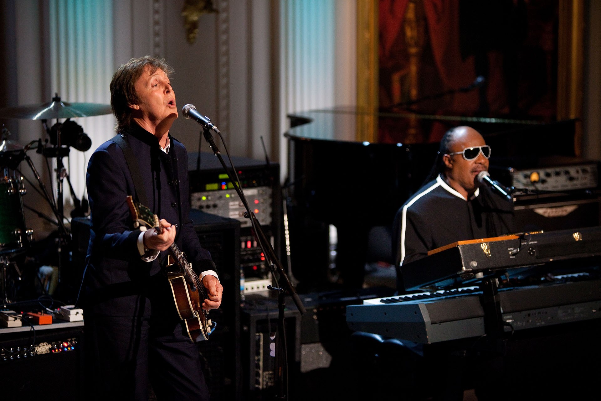 Paul McCartney und Stevie Wonder treten gemeinsam bei den Grammys auf, wobei McCartney Gitarre spielt und singt und Wonder eine Brille trägt, während er am Piano spielt.