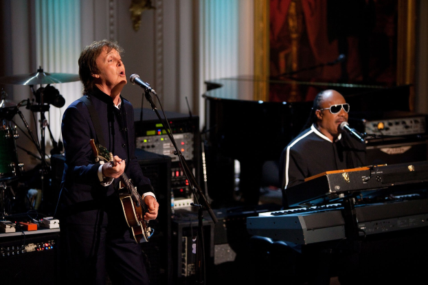 Paul McCartney und Stevie Wonder treten gemeinsam bei den Grammys auf, wobei McCartney Gitarre spielt und singt und Wonder eine Brille trägt, während er am Piano spielt.