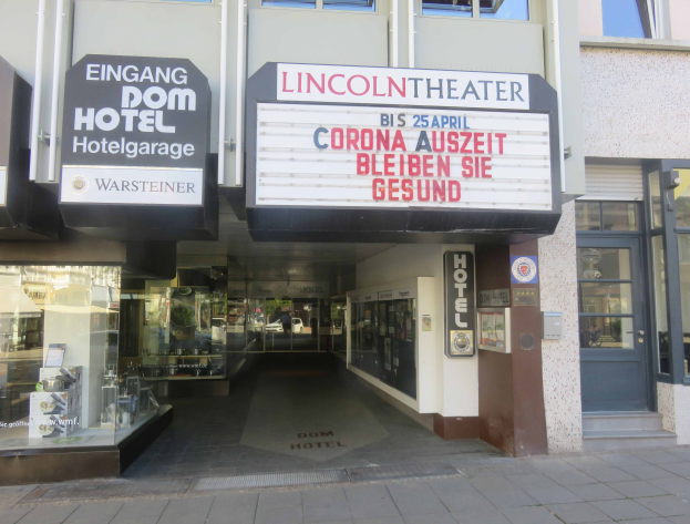 Das Lincoln Theater in Berlin, Deutschland, ein Gebäude mit Glasfenstern und -türen sowie einer Tafel mit Text darauf, das verschiedene Gegenstände im Inneren zeigt und so einen belebten Stadtblick bietet.