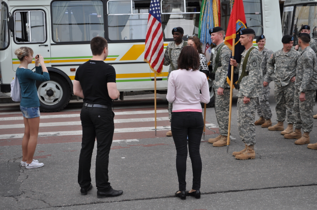 Eine Gruppe von Menschen steht auf einer Straße mit einem Bus, Taschen, Fahnen und verschiedenen Gegenständen.