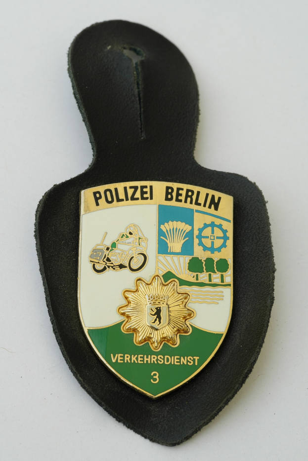 Ein Polizeiabzeichen von Berlin mit einem blauen Schild, einem weißen Stern und schwarzer 'Polizei Berlin'-Aufschrift auf einer Oberfläche.