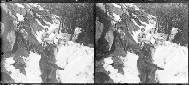 Schwarzes und weißes Foto von Menschen in Winterkleidung, die mit Geweihen versehene Pferde durch unberührten Schnee reiten, mit Bäumen und Felsen im Hintergrund.