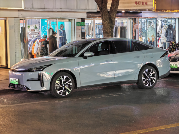 Ein Mitsubishi Lancer EV, das nachts auf einer Straße geparkt ist, umgeben von Gebäuden, Geschäften, Schaufensterpuppen, Schildern und Lichtern.