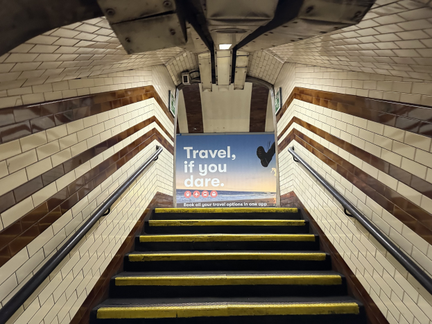 Eine Treppe in einer U-Bahn-Station mit einem 'Reise, wenn du wagst'-Schild oben, flankiert von Geländern und sichtbaren Stationswänden.