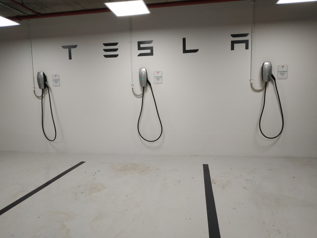 Eine Tesla-Ladestation in einer Parkgarage mit angebrachten Kabeln und Deckenbeleuchtung, die die darunterliegende Etage zeigt.