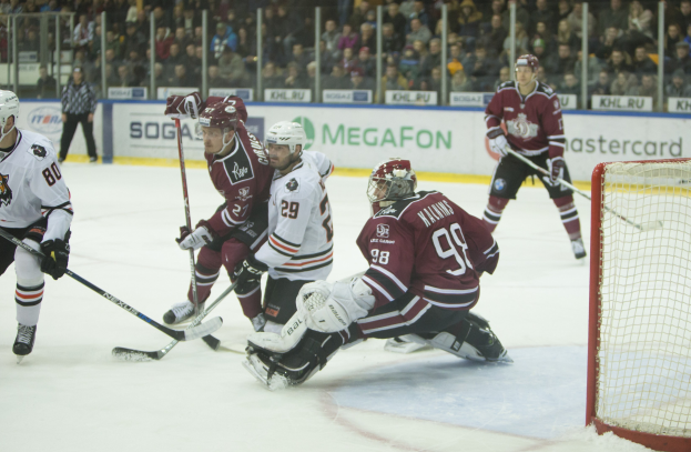 Gruppe von Menschen, die Hockey auf einem Eisstadion mit Helmen, Hockey-Schlägern, einem Torpfosten auf der rechten Seite und Zuschauern in den Tribünen mit Bannern im Hintergrund spielen.