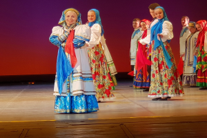 Eine Gruppe von Menschen in farbenfrohen, detaillierten traditionellen ukrainischen Kostümen, die auf einer Bühne lächeln.