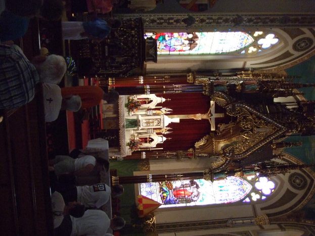 Ein Innenblick in eine Kirche mit einem Kreuz, das eine Jesus-Skulptur und zahlreiche Personen auf Stühlen vor sich zeigt.