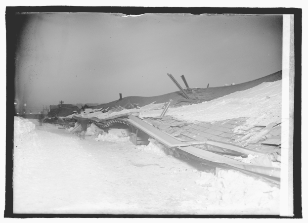 Ein Schwarz-Weiß-Foto eines teilweise eingestürzten Dachs mit Schnee auf dem Boden und Pfählen im Hintergrund.