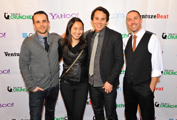 Eine Gruppe strahlender Menschen, die mit einem Sponsorenbanner im Hintergrund für die Kamera posen.