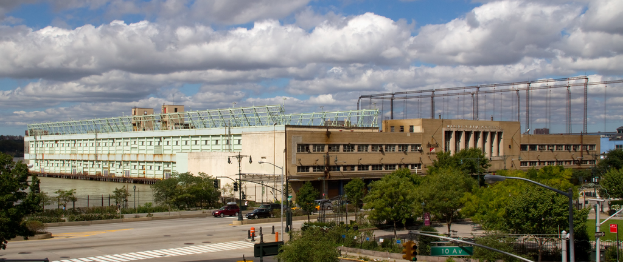 Eine Straße mit Fahrzeugen, Bäumen und Straßenlaternen, die zu einem großen Gebäude neben einem Gewässer führt.