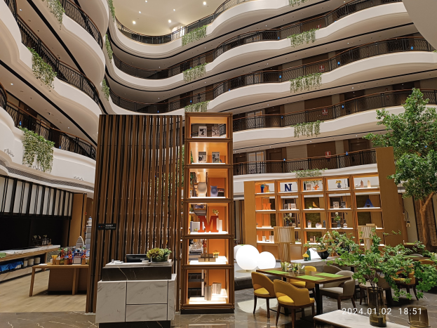 Großer Innenhof mit Tischen, Stühlen, Zimmerpflanzen, Geländern und Beleuchtung, als Hotelinnere in Dubai, VAE, bezeichnet.