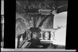 Ein Schwarz-Weiß-Foto eines Kirchenpults mit geschnitzten Säulen und einer texturierten Wand im Hintergrund.