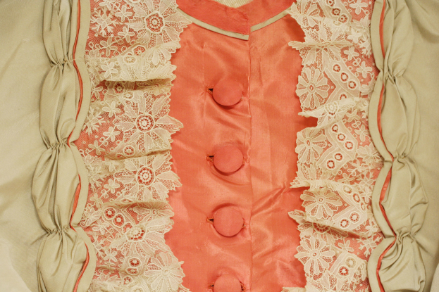 Nahaufnahme eines rosafarbenen und cremefarbenen Kleides mit weißer Spitzenborte und vorderen Knöpfen.