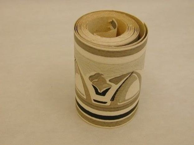 Ein zylindrischer hellbrauner Karton-Toilettenpapier-Rollen mit leichten Knittern sitzt auf einem glatten hellholzbefarbenen Tisch.