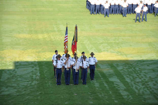 Eine Gruppe von Jungen in weißen und blauen Kleidern steht auf einem grünen Feld, einige halten Fahnen in der ersten Reihe und andere stehen in Reihen dahinter.
