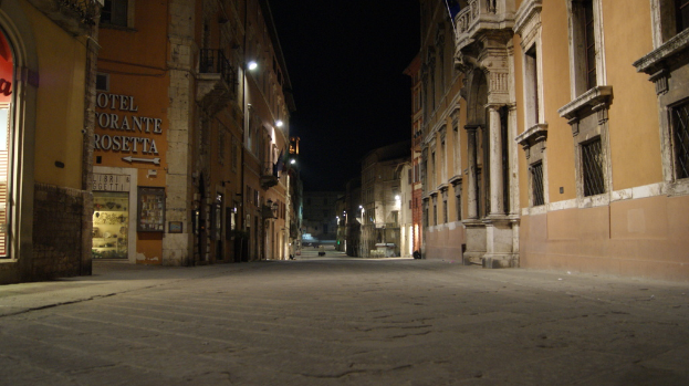 Eine Nachtaufnahme einer Stra├če mit Geb├Ąuden auf beiden Seiten und einem Laden auf der linken Seite sowie Lichtern in der Mitte.