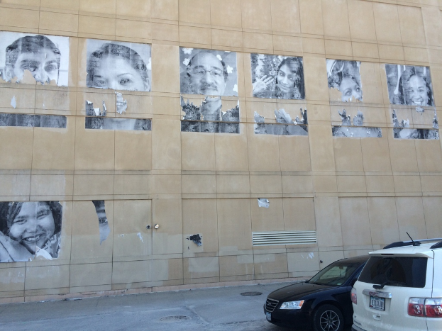 Ein Gebäude mit Autos auf der Straße davor, das Manhole-Deckel und Plakate von Menschen an der Wand im Hintergrund zeigt.