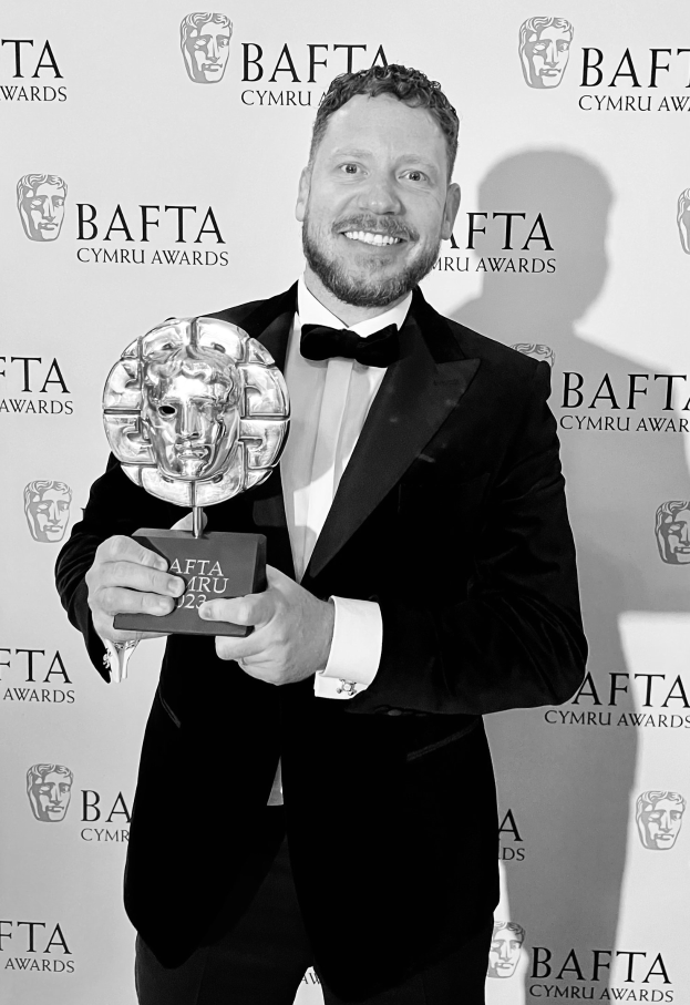 Ein Mann in einem Smoking, der eine BAFTA-Trophäe hält und lächelt, mit einer Hintergrundtafel, auf der "BAFTA Awards 2018" steht