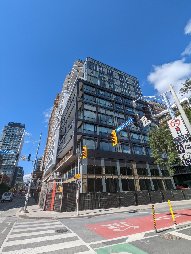 Eine belebte Stadtstraße mit einem hohen Wohn-/Geschäftshaus zum Verkauf an der 541 East 57th Street, Unit 541, Ampeln, Fahrzeuge, Schilder, Bäume, ein Zaun.