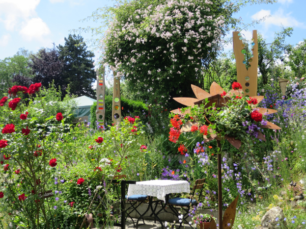 Ein Garten mit farbenfrohen Blumen und Pflanzen, der einen Tisch mit einer Decke und Stühlen in der Mitte zeigt, umgeben von Bäumen unter einem bewölkten Himmel auf der Chelsea Flower Show.