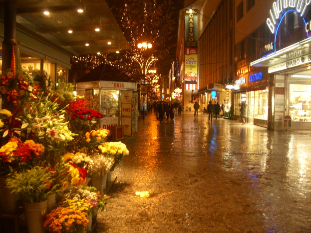 Eine Straßenszene mit Blumensträußen, Menschen, die gehen, beleuchteten Gebäuden, Werbetafeln und Werbung.