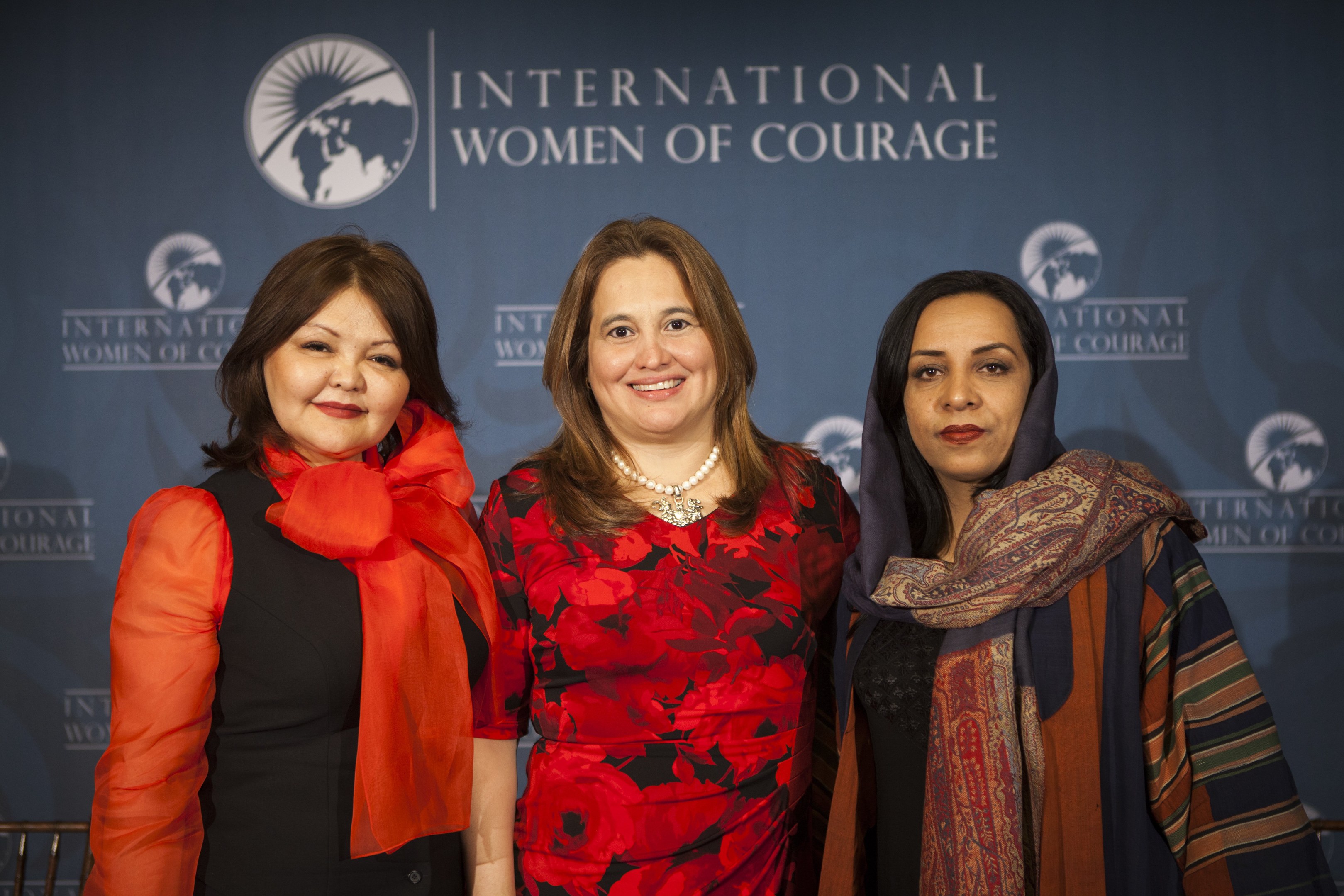 Drei Frauen lächeln vor einem 'Internationale Frauen des Mutes' Banner