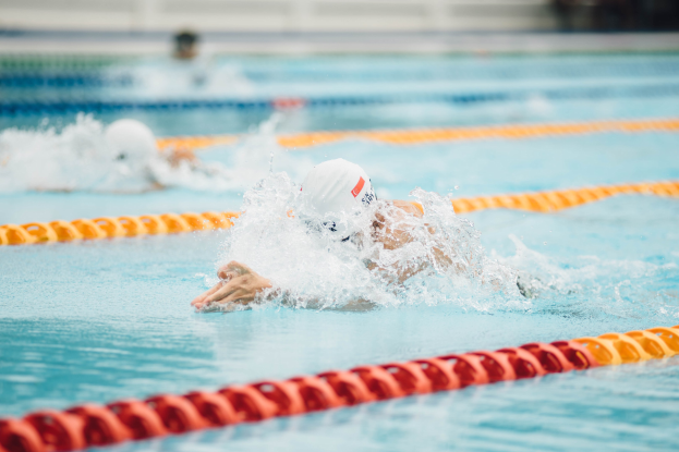 Zwei Schwimmer in einem Rückenschwimmwettbewerb mit ausgestreckten Armen in einem Schwimmbecken; Hintergrund ist unscharf.