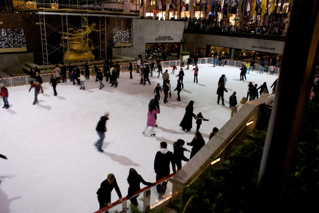 Eine Gruppe von Menschen, die auf einer zugefrorenen FlÃ¤che Eiskunstlauf betreiben, umgeben von GebÃ¤uden.