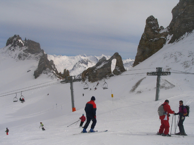 Menschen in Pullovern fahren mit Skiern auf dem Eis mit einer Seilbahn, Bergen und einem bewölkten Himmel im Hintergrund.