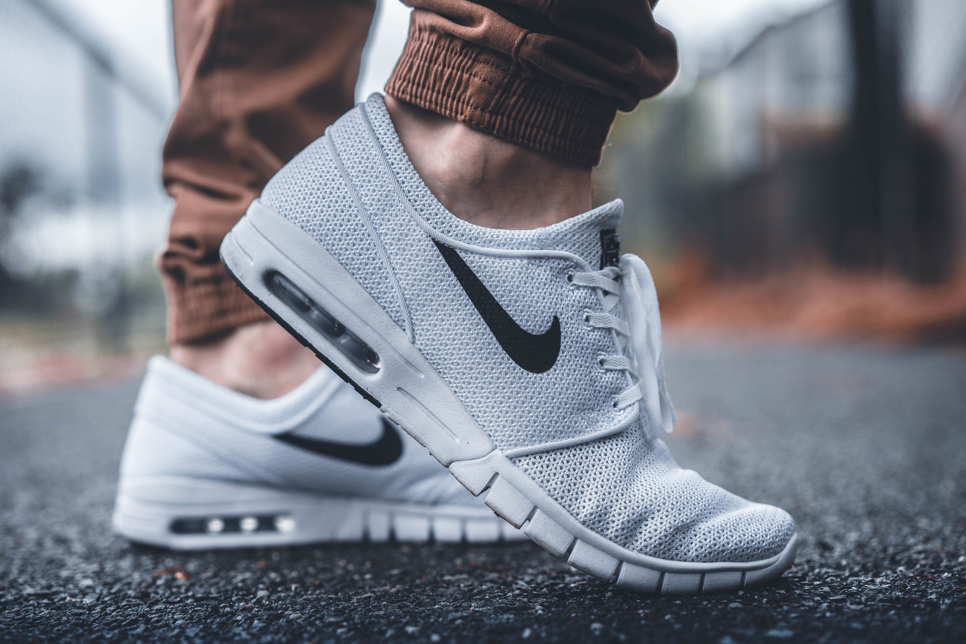 Nahaufnahme einer Person in schwarzen, weißen und grauen Nike SB Stefan Janoski Max-Schuhen vor einem unscharfen, träumerischen Hintergrund.