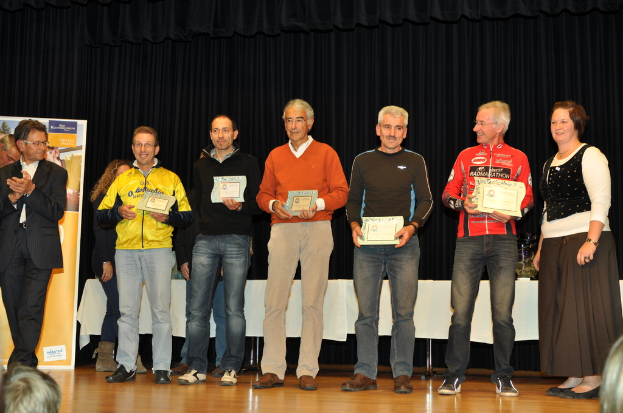 Eine Gruppe von Menschen steht auf einer Bühne und hält Zertifikate in der Hand, im Hintergrund ist eine Wand zu sehen, daneben ein Tisch und ein schwarzer Vorhang.