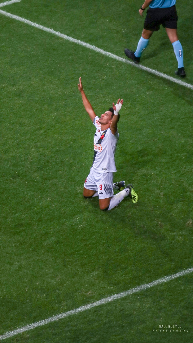 Ein Fußballspieler kniend auf dem Boden mit ausgestreckten Armen in Feierlaune, tragend einen Sportanzug und Fußballschuhe.
