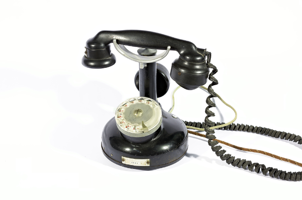 Ein schwarzes Telefon mit Zahlen und Text, der durch seine Glasfront sichtbar ist, verbunden durch Kabel, vor einem weißen Hintergrund.