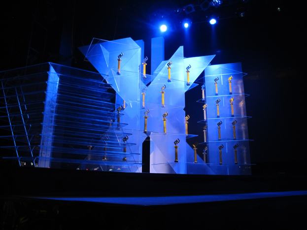 Eine Bühne für eine Preisverleihung mit dunklem Hintergrund, ein paar Lichtern und einigen Gegenständen, die mit dem Event in Verbindung stehen.