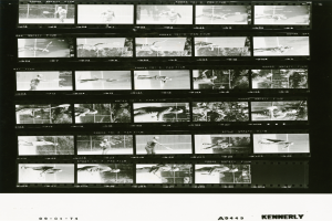 Ein Schwarz-Wei├č-Foto eines Mannes, der Tennis spielt, mit einem wei├čem Hemd und Shorts, der einen Schl├Ąger in der rechten Hand h├Ąlt, mit konzentriertem Gesichtsausdruck und einem Filmstreifen im Hintergrund.