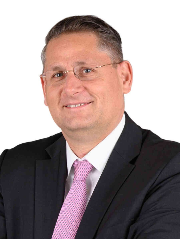 Ein Mann im Anzug und Krawatte, der eine Brille trägt, lächelt in die Kamera vor einem weißen Hintergrund, was darauf hindeutet, dass er ein Finanzberater ist.