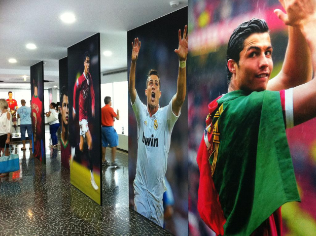 Ein Banner mit dem Fussballspieler Rolando, umgeben von Menschen, die links neben einem Tisch stehen und Lichter an der Decke.