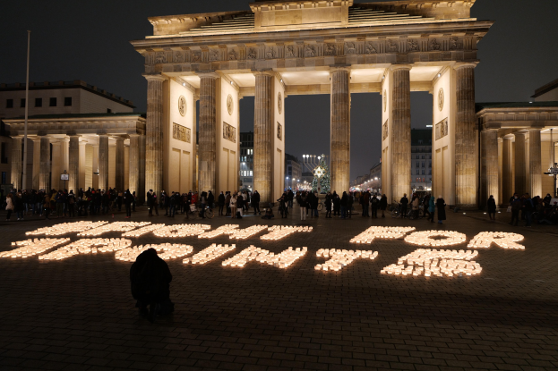 Eine Gruppe von Menschen steht vor dem beleuchteten Reichstag in Berlin, Deutschland, umgeben von Gebäuden, Masten und Lichtern; die Worte 'Kampf für Freiheit' sind im Vordergrund auf dem Boden zu sehen.