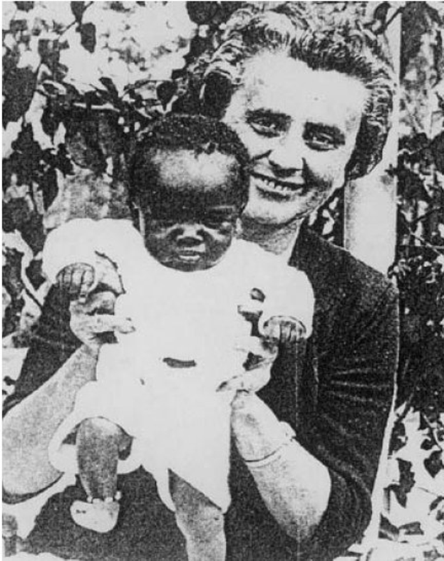 Ein Schwarz-Weiß-Foto einer Frau, die strahlend lächelt, während sie ein Baby hält, mit Blättern im Hintergrund.