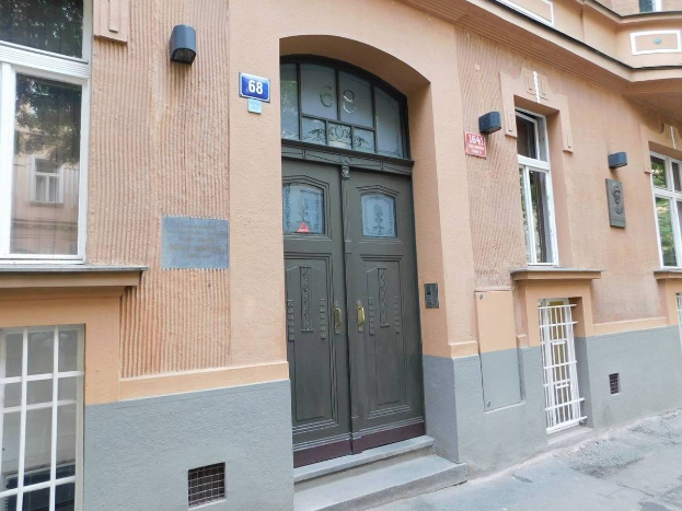 Ein zweistöckiges Gebäude mit einer grünen Tür und Fenstern, das Schilder und Lichter an seiner Wand hat und sich auf einer städtischen Straße mit einem Fußweg befindet, der zu ihm führt und als Wohnung zum Verkauf angeboten wird.