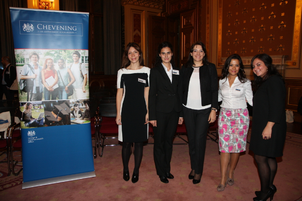 Ein Banner auf der linken Seite, Stühle im Hintergrund, fünf Frauen auf der rechten Seite und eine Wand im Hintergrund.