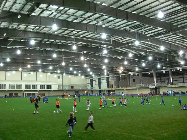 Ein Hallenfußballstadion mit einer Gruppe von Menschen, die auf dem Feld Fußball spielen, Torpfosten und Deckenbeleuchtung.