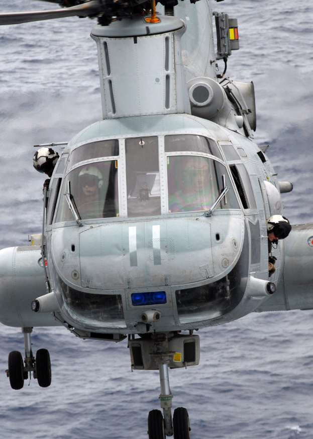 Ein Helikopter mit zwei Helmträgern darin, der über das Meer fliegt.