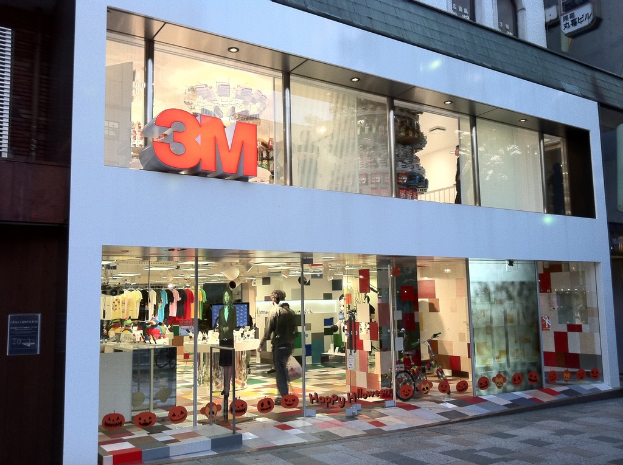 Ein Gebäude mit einer Glaswand, auf der Kleider an Bügeln, eine Schaufensterpuppe, ein Fahrrad, angeklebte Bilder und Schrift auf der Glaswand zu sehen sind.