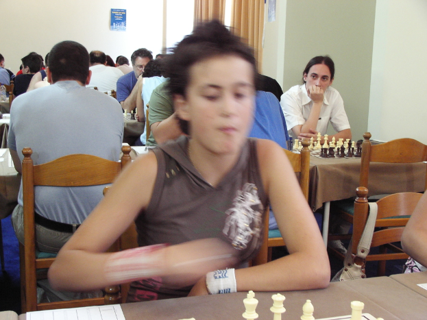 Ein Raum mit Menschen an Tischen Schach spielend, mit einer Vorhangwand und einem Foto in der Ecke.