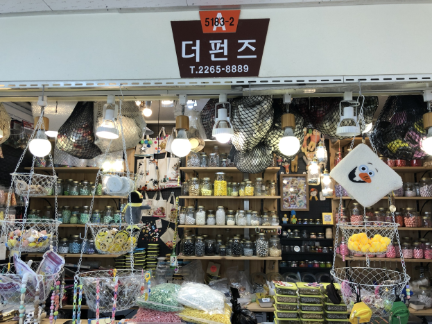 Ein unordentlicher Laden in Seoul zeigt verschiedene Gegenstände wie Körbe, Lampen, Flaschen und Spielzeuge auf Regalen, mit einer Tafel oben, die anzeigt, dass es einer der besten koreanischen Läden ist.