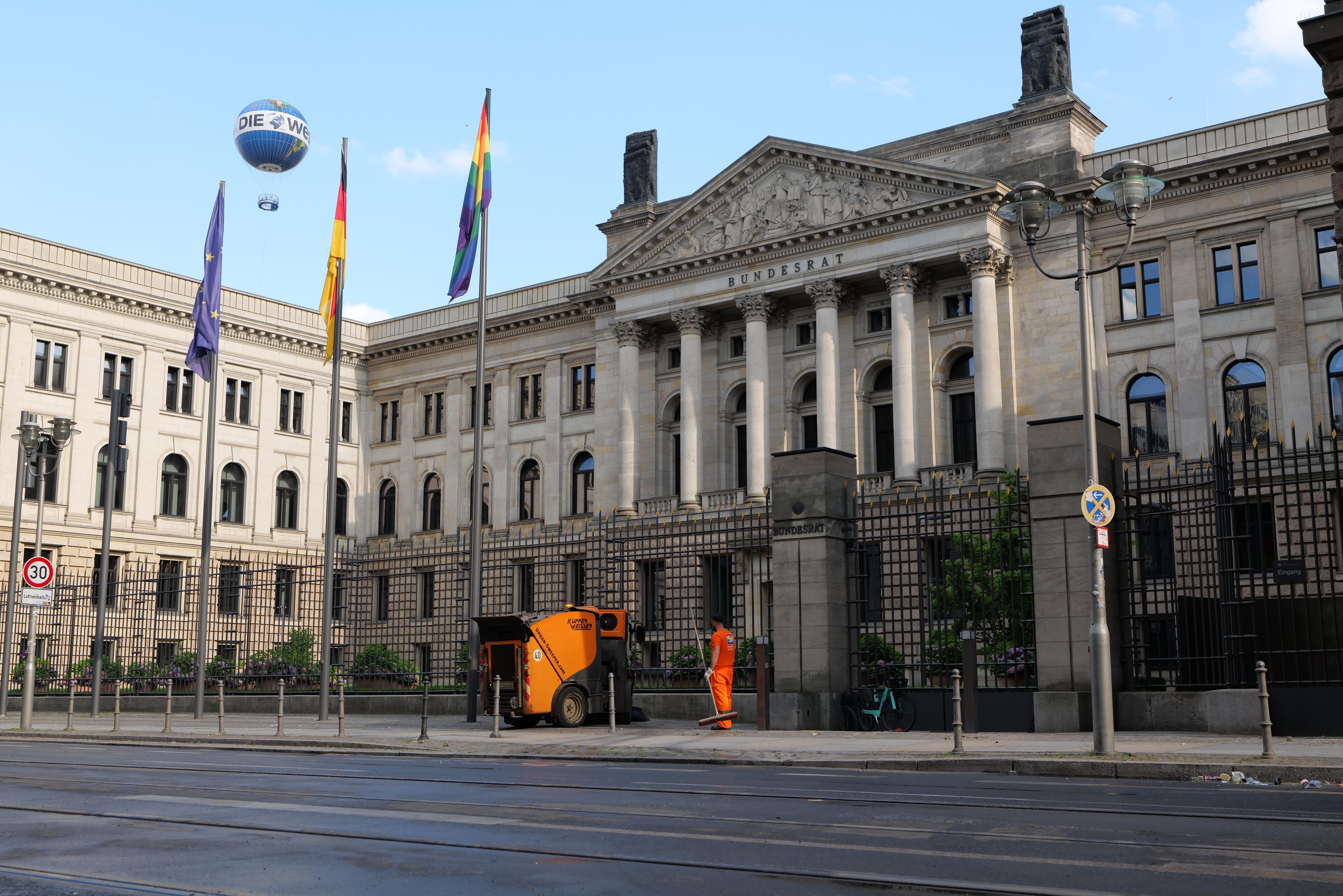 Großes modernes Gebäude mit zahlreichen Fenstern, identifiziert als der Bundestag in Berlin, Deutschland, umgeben von Straßeninfrastruktur, Fahrzeugen, Passanten und Bäumen unter einem bewölktem Himmel.